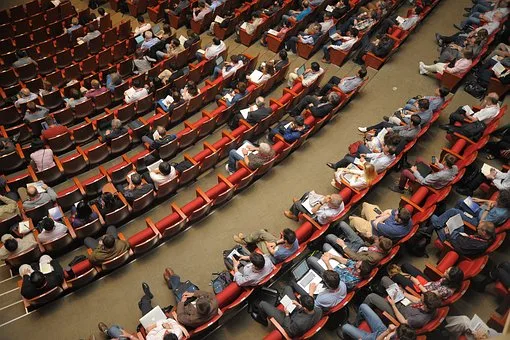 Auditorio grande para conferencias vista desde arriba, en la que ya se encuentran algún asistentes.