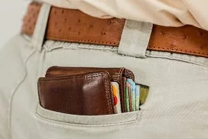 Imagen de una cartera que se asoma del bolsillo trasero de un pantalón, en la que se ven una tarjeta de crédito y varios billetes.