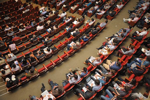 Auditorio grande para conferencias vista desde arriba, en la que ya se encuentran algún asistentes.